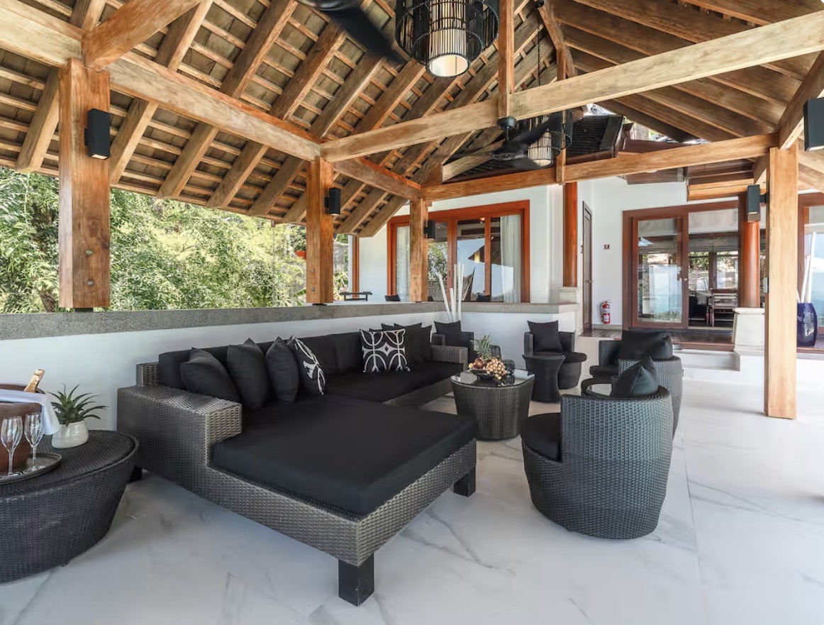Open-air sala lounge with black rattan sofas under a timber roof