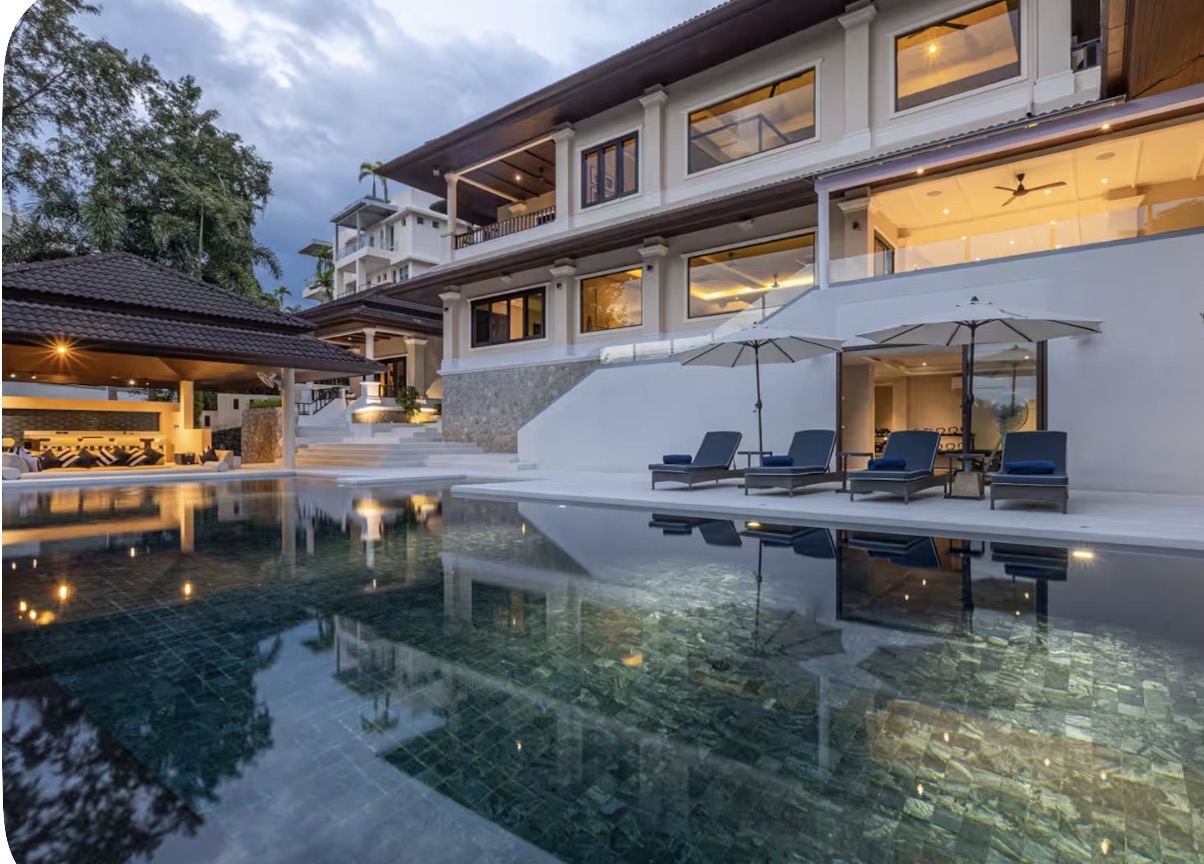 The Phuket villa lit up at dusk beside its reflecting pool